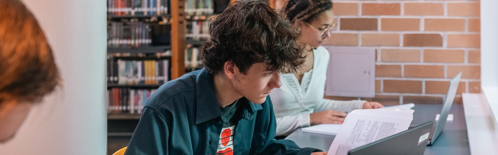 Teenagers studying textbooks and working on laptops