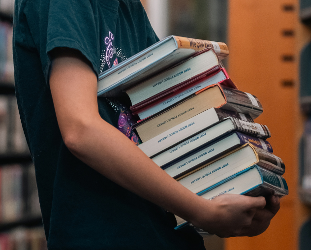 Child holding a tall stack of books